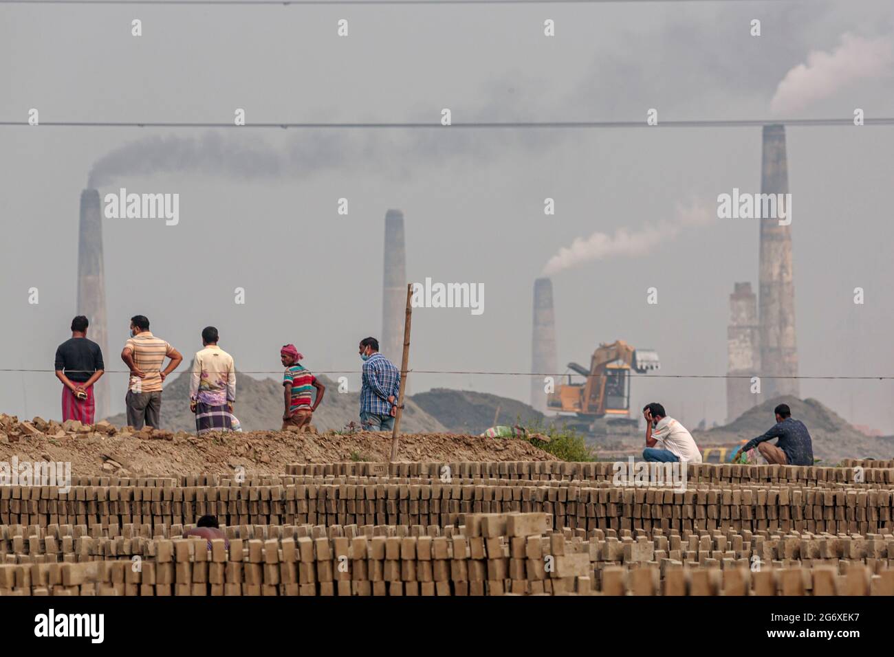 Persone in piedi in un campo di mattoni, guardando fuori su altri forni di mattoni nella zona di Ashulia in Bangladesh. A causa dell'elevata domanda di materiali da costruzione a basso costo, la produzione di mattoni in argilla è diventata un'industria fiorente in Bangladesh, con forni di produzione fortemente concentrati nelle periferie delle città più grandi. Questi siti di produzione, noti come brickfields, operano utilizzando tecnologie secolari che espellono polvere, cenere, fumo nero e altre sostanze inquinanti nell'atmosfera Foto Stock