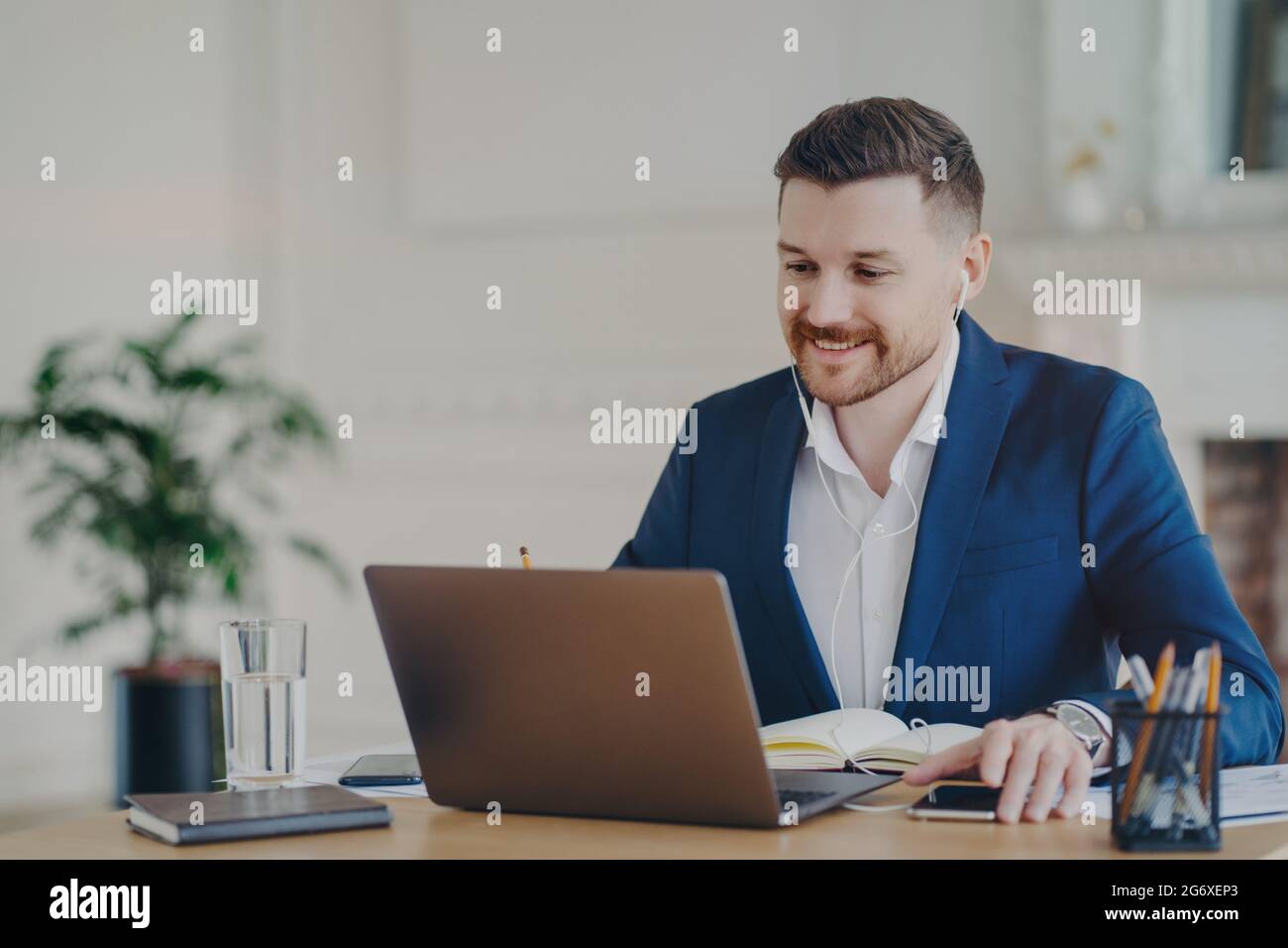 Un manager sorridente che indossa auricolari e incontra online i dipendenti Foto Stock