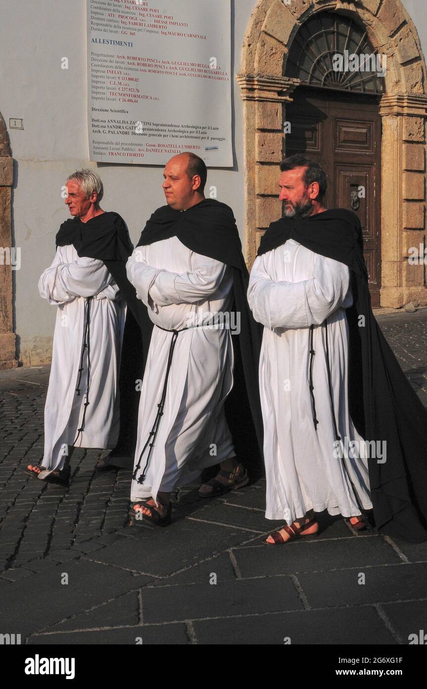 Il miglior piede avanti ... un trio sacerdotale vestito da monaci  cistercensi cattolici medievali cammina in fila con le braccia ripiegate  attraverso Piazza Guglielmo Marconi ad Anagni, Lazio, Italia, in una storica