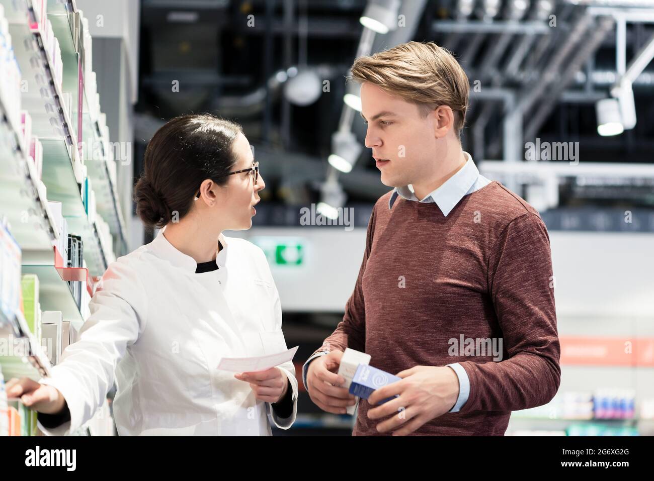 A basso angolo di visione di un bel giovane azienda due farmaci prescritti mentre guardando diversi prodotti farmaceutici in una farmacia moderna con lui Foto Stock