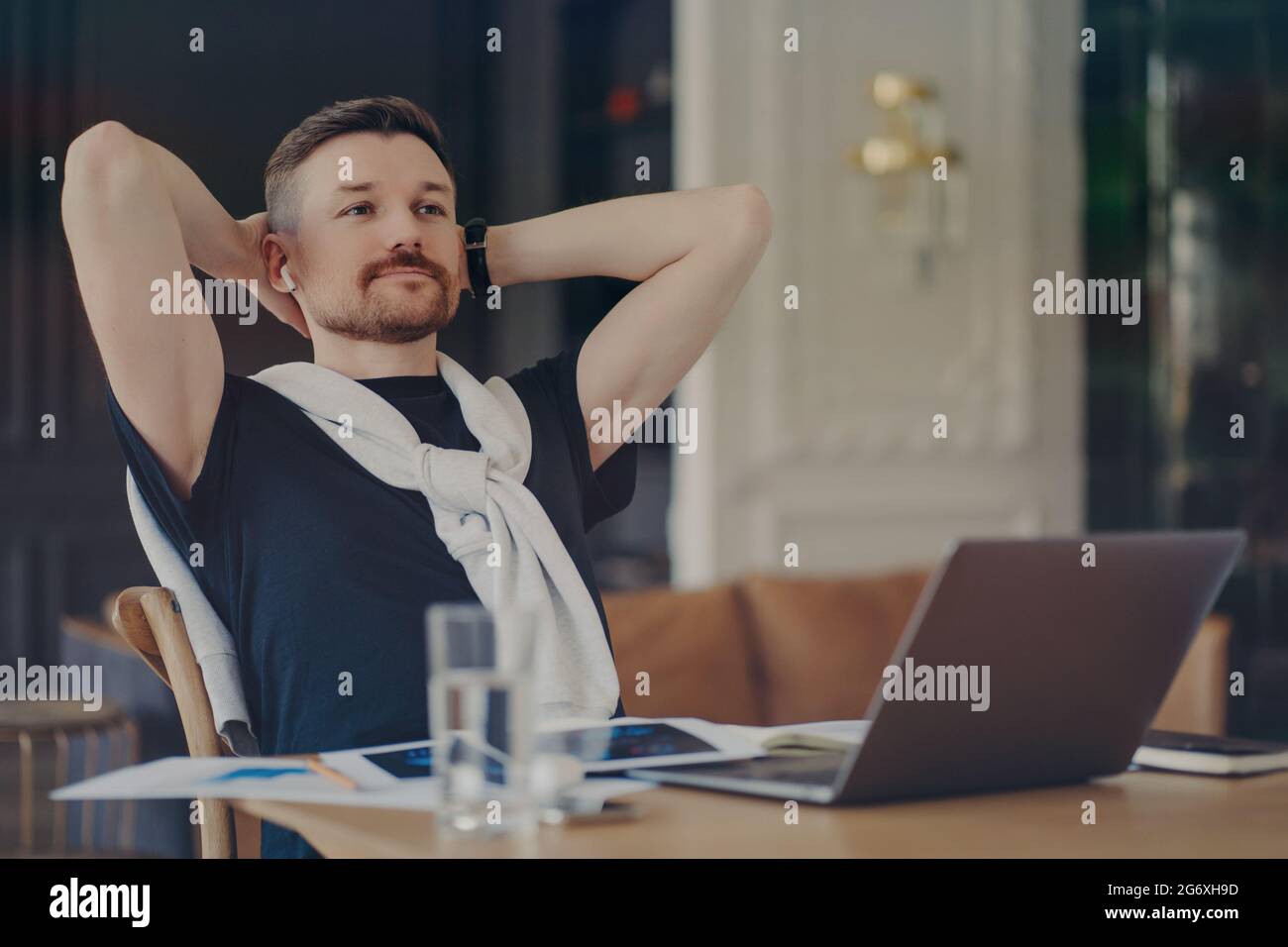 L'uomo pensante bearded in attività tiene le mani dietro la testa si siede al desktop con i moderni gadget pensa al lavoro a distanza concentrato in distanza Foto Stock