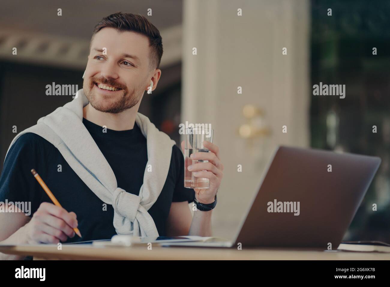 Bell'uomo d'affari in un abbigliamento casual con un bicchiere d'acqua che lavora in un ufficio moderno Foto Stock