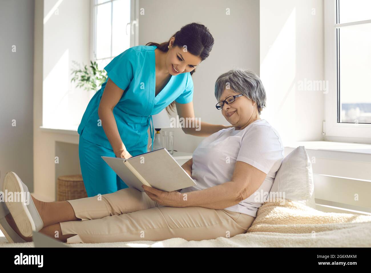 Caregiver in una casa di cura discute un libro che una donna più anziana sta leggendo mentre si trova a letto. Foto Stock