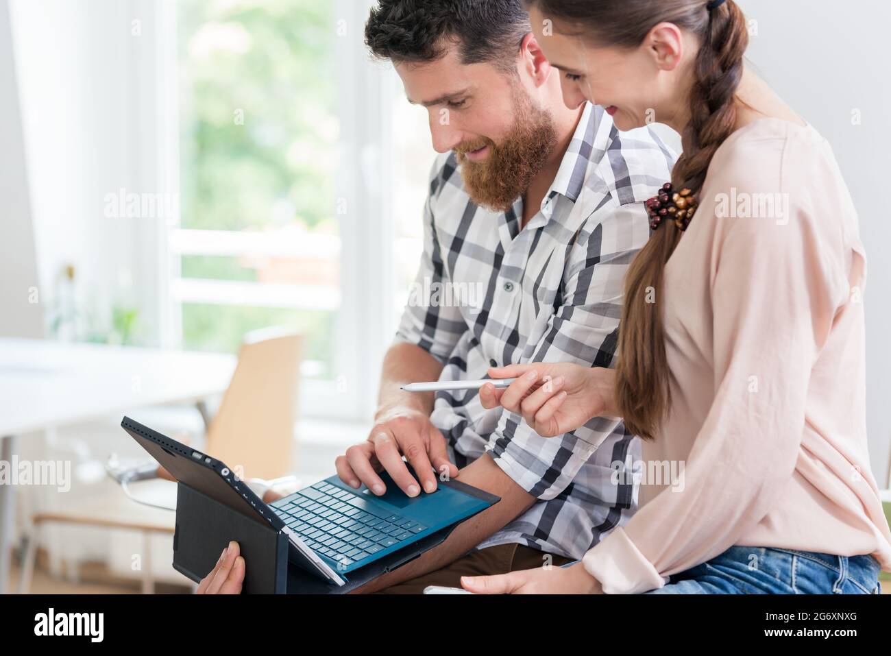 Giovane allegro che usa un tablet con tastiera e connessione wireless a Internet, mentre collabora con la sua collega femminile in un lavoro condiviso Foto Stock