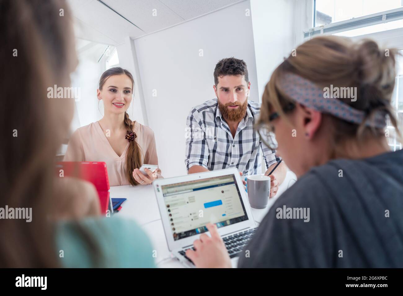 Giovani collaboratori affidabili che pensano alle soluzioni e alle nuove idee di successo condividendo la scrivania di un moderno spazio d'ufficio per i nomadi digitali Foto Stock