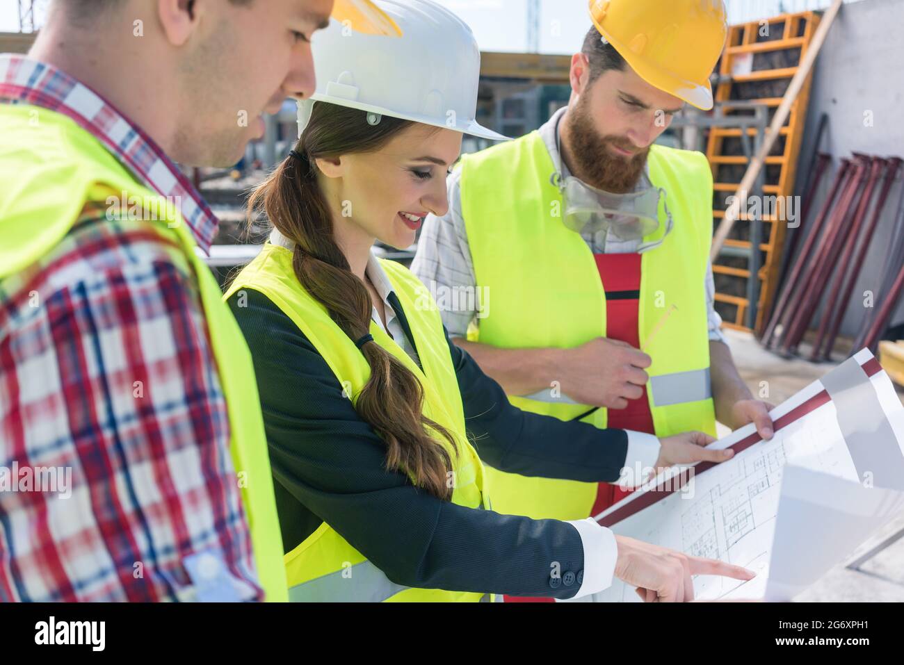 Giovani e fiducioso architetto femmina sorridere mentre la condivisione di idee circa il piano di un edificio in costruzione all'aperto con due operai Foto Stock