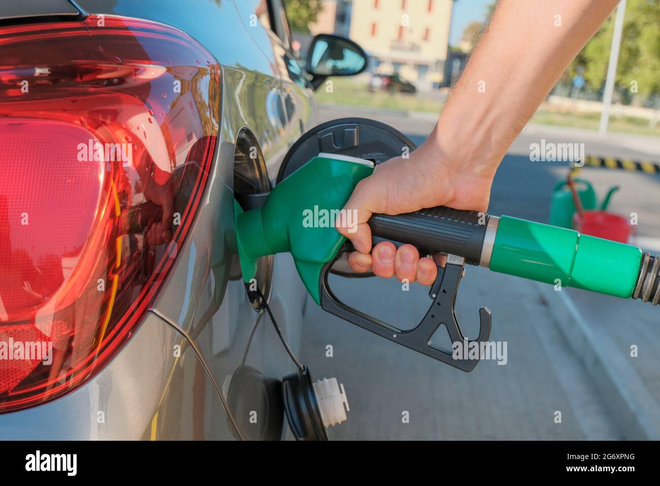 Le mani dell'uomo tengono la pompa di benzina e riempiono l'auto di carburante da vicino attraverso le strade della città. Industria energetica. Stazione di benzina business / mercato. Foto Stock
