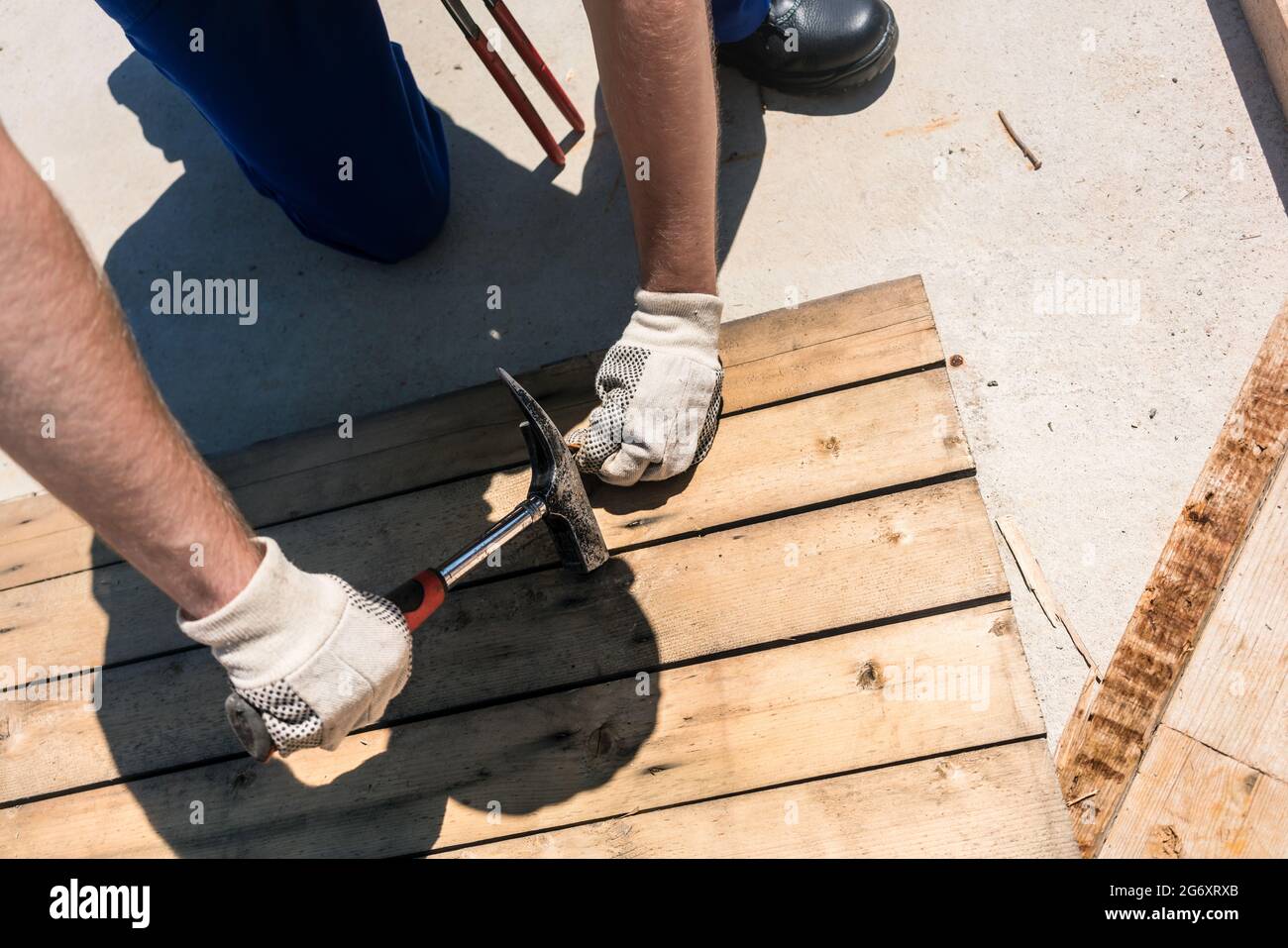 Vista ad alto angolo di un operaio con collare blu che indossa elmetto giallo, giubbotto di sicurezza e guanti mentre si utilizza un martello durante il lavoro sul cantiere Foto Stock