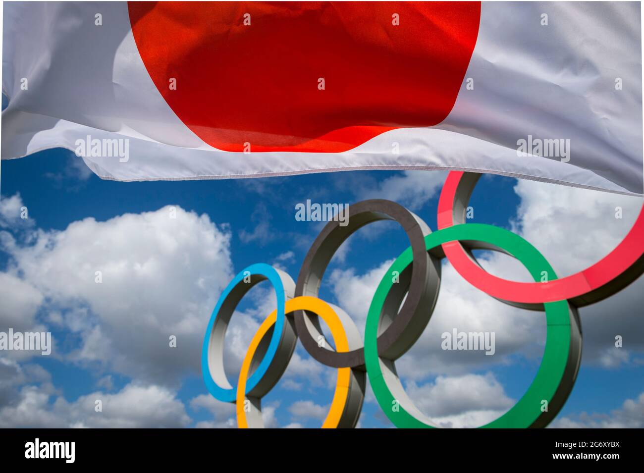 RIO DE JANEIRO - MARZO, 2016: Una bandiera giapponese svanita nel vento davanti agli anelli olimpici che si ergono sotto il cielo azzurro. Foto Stock