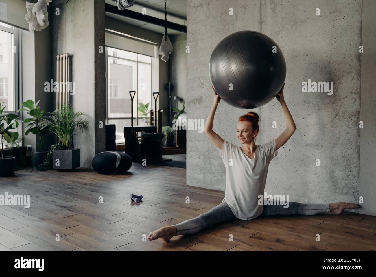 Bella donna fitness in posizione divisa tenendo la palla di esercizio sopra la testa e godendo di allenamento pilates Foto Stock