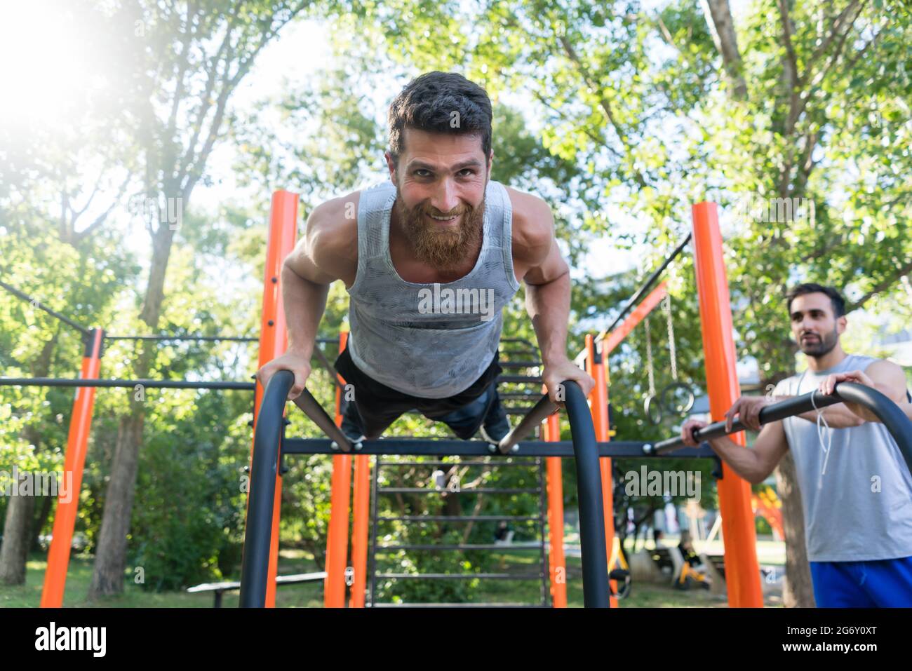 A basso angolo di visione di un barbuto atletica giovane uomo facendo push-up su barre parallele orizzontali durante l'allenamento all'aperto in un moderno parco fitness Foto Stock