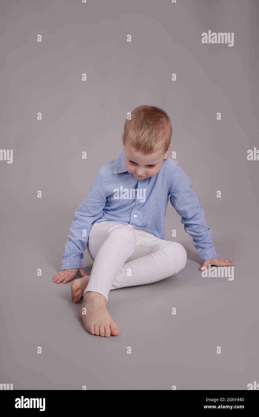 piccolo e affascinante ragazzo prescolare con pantaloni bianchi e camicia  blu su sfondo grigio. bambino, bambino Foto stock - Alamy