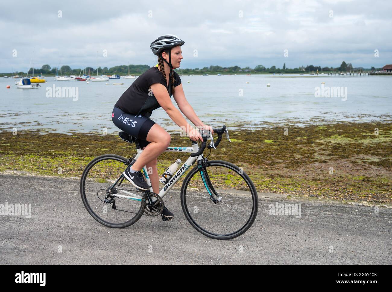 Vista laterale di una giovane donna in bicicletta o in bicicletta che indossa un casco in West Sussex, Inghilterra, Regno Unito. Foto Stock