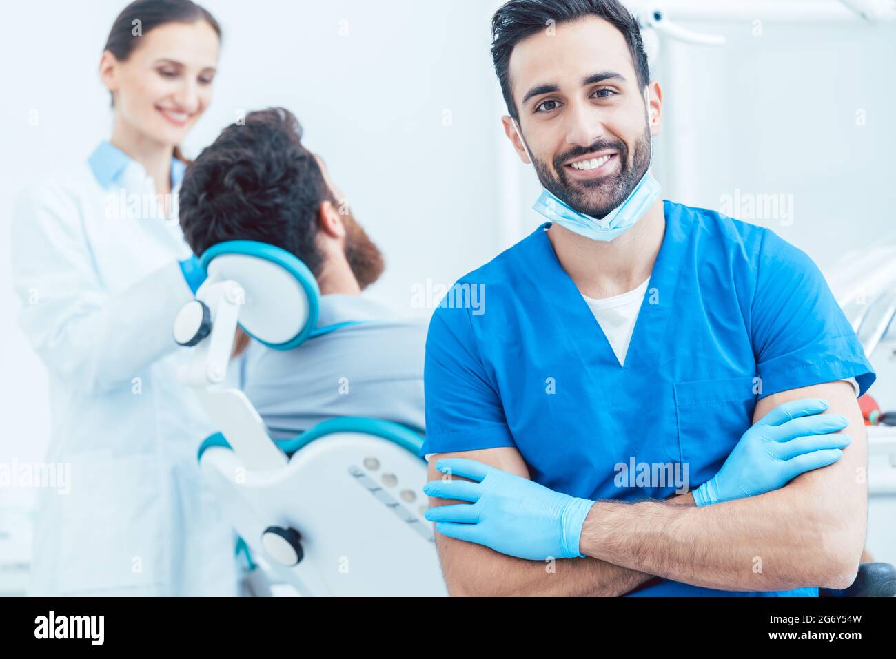 Ritratto di un sicuro chirurgo dentale indossando uniforme protettiva blu e maschera chirurgica mentre si guarda la fotocamera in un moderno studio dentistico con reliab Foto Stock