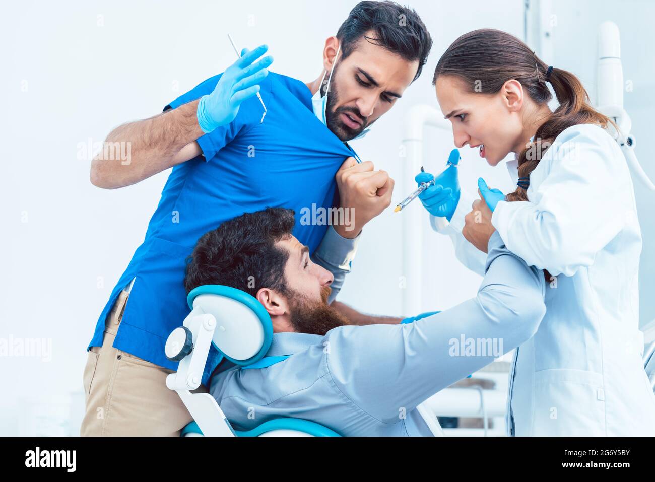 A basso angolo di visione di un divertente di dentista o di dentista deliberando pazzo davanti al suo assistente femmina, pur avendo un paziente su sedia nel dentale o Foto Stock