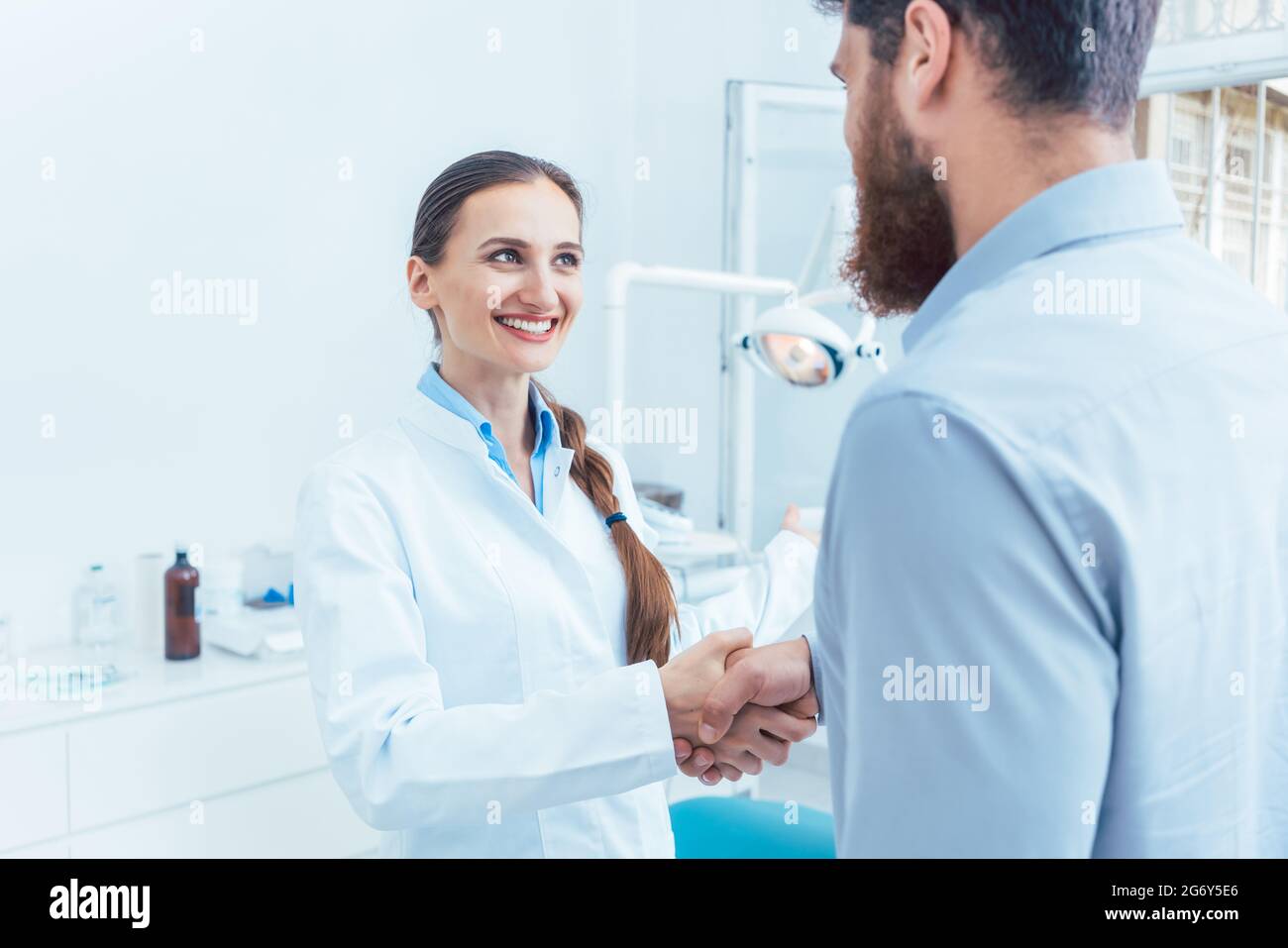 Ritratto di un affidabile e allegra femmina di dentista o di dentista agitando la mano di un paziente nello studio dentistico di una moderna clinica Foto Stock