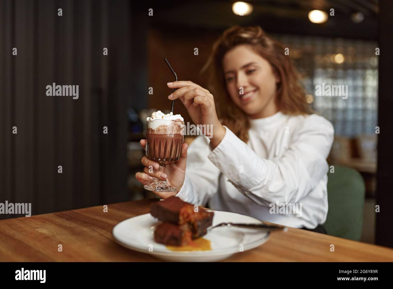 Donna sorridente che mangia gustoso dessert e beve cacao Foto Stock