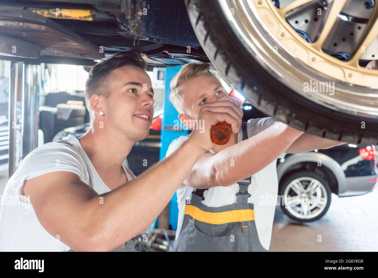 Due dedicate auto tuning meccanica di una macchina attraverso la modificazione dei cerchi, mentre si lavora insieme in una moderna automobile repair shop Foto Stock