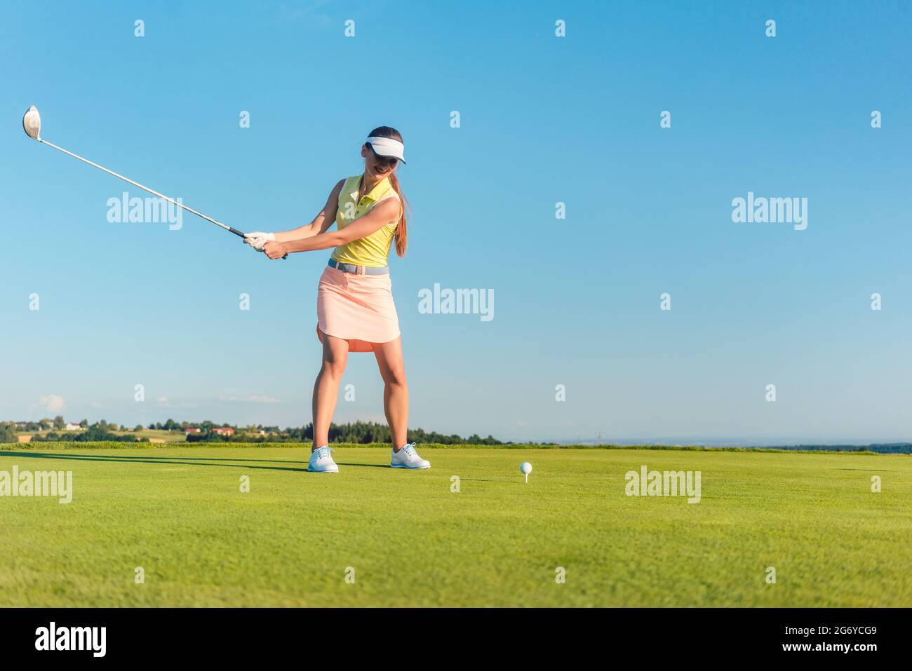 Lunghezza completa di un professionista di golf femminile player sorridente durante l'oscillazione un driver club con concentrazione e precisione prima di colpire la palla durante i Foto Stock