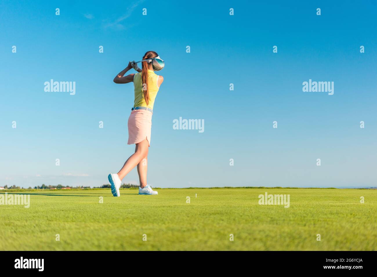 Lunghezza completa di un professionista di golf femminile player sorridente durante l'oscillazione un driver club con concentrazione e precisione prima di colpire la palla durante i Foto Stock