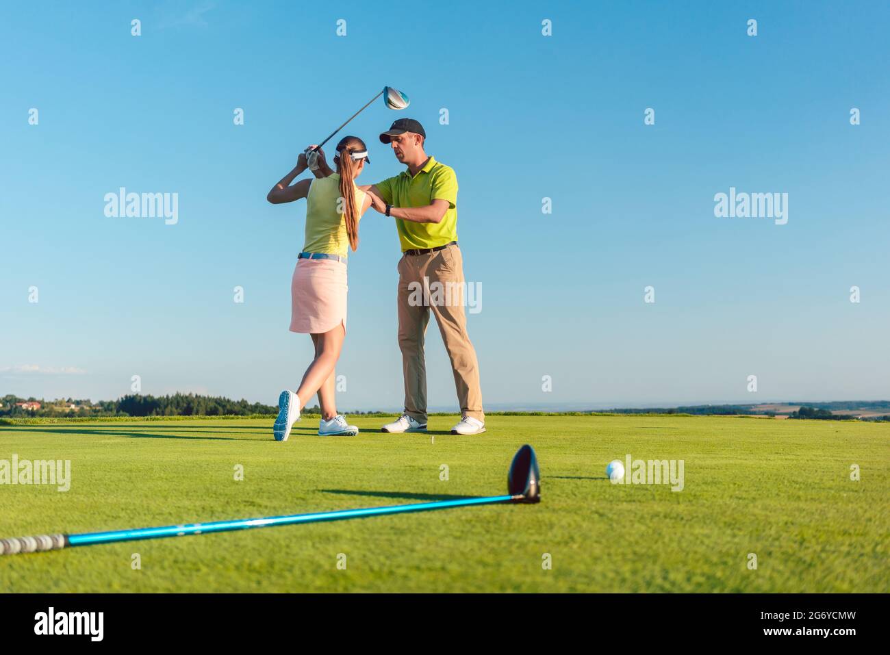 La lunghezza completa di un istruttore di golf esperto che insegna ad una giovane donna di swing il randello dell'autista per un colpo professionale, durante la classe per i principianti all'aperto Foto Stock