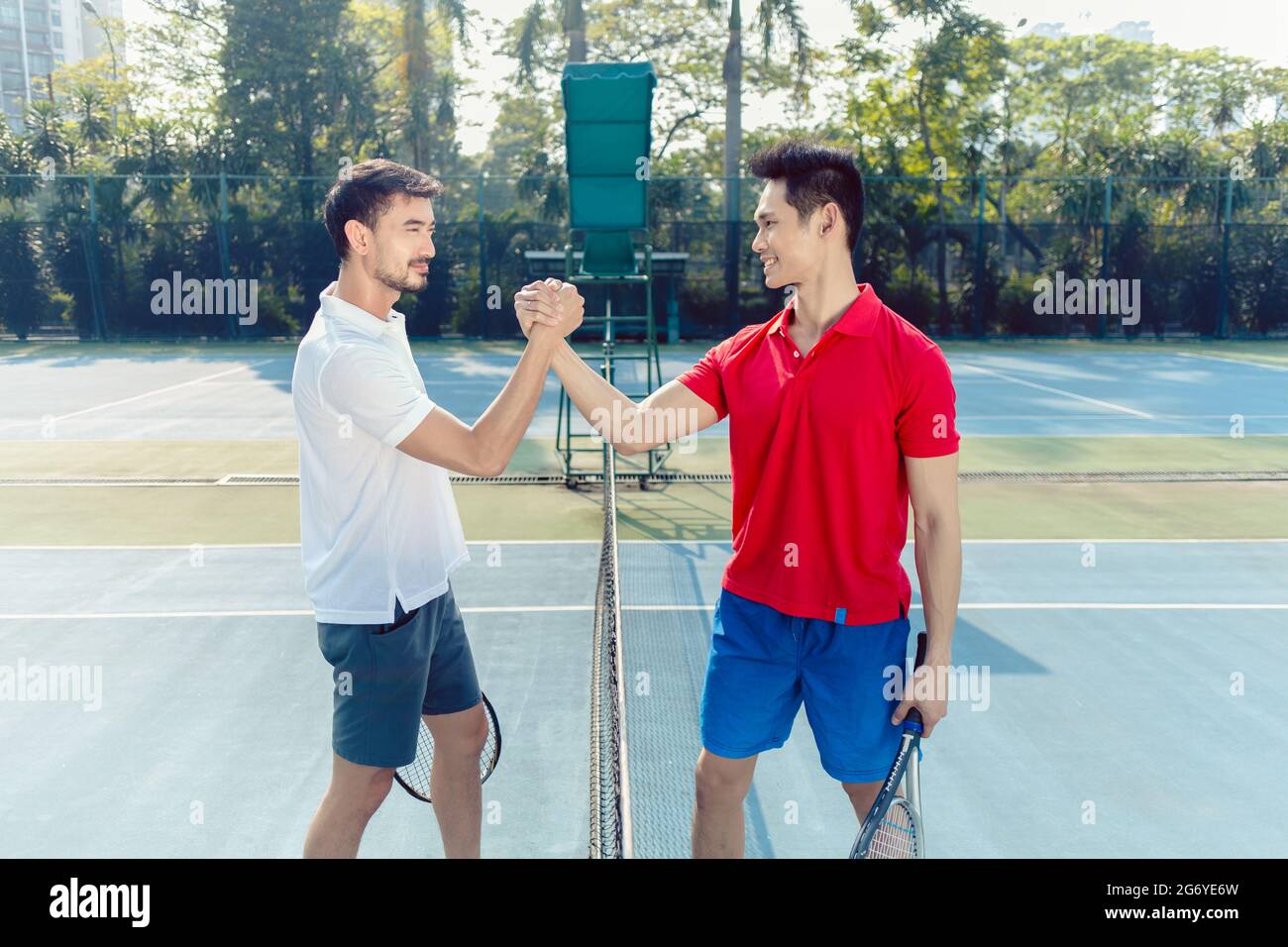 Vista laterale di due giocatori di tennis professionisti che scuotono le mani sopra la rete come un gesto di fair play prima di iniziare la partita Foto Stock