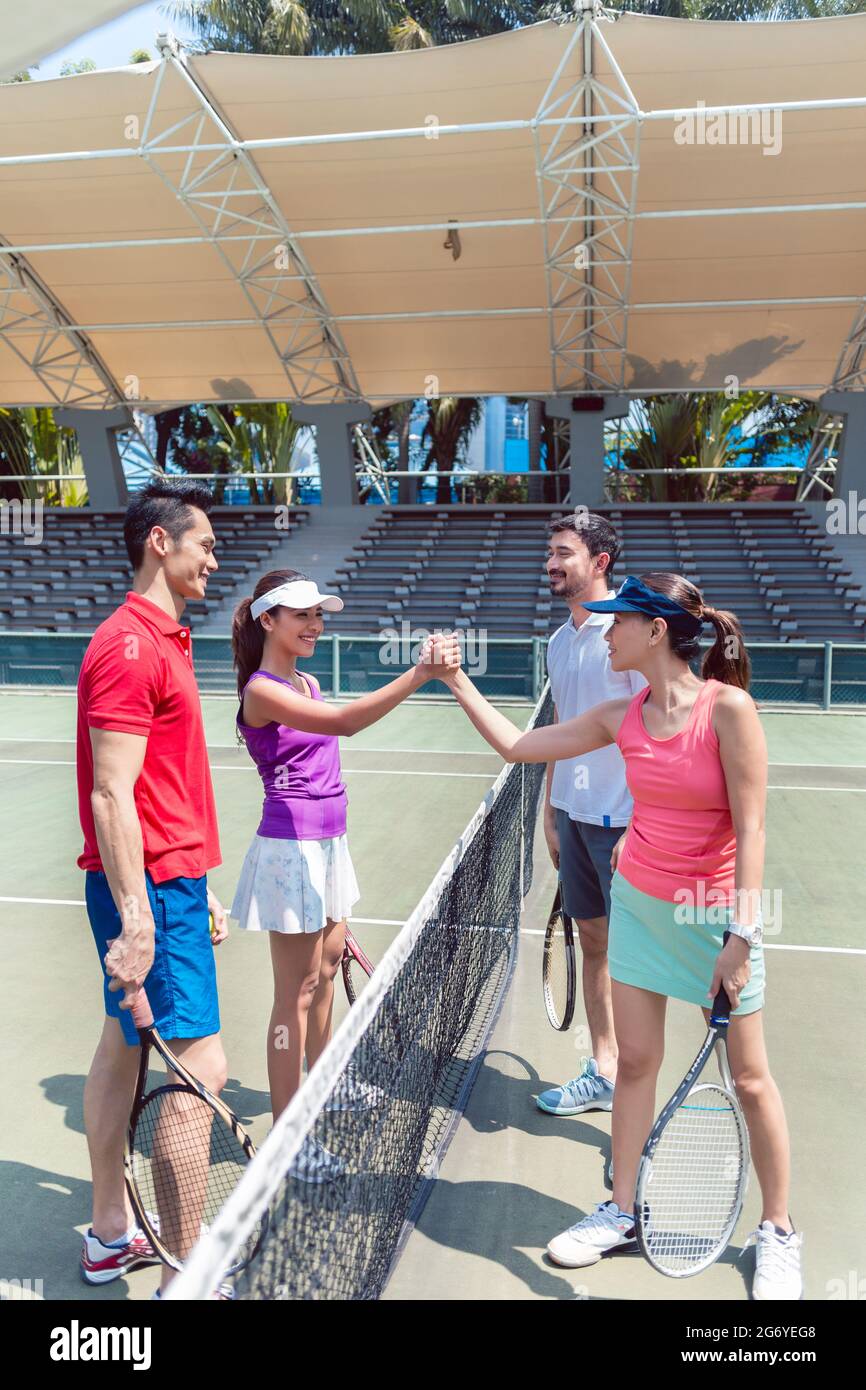 Quattro giovani e competitivi i giocatori di tennis di mettere le mani insieme al di sopra della rete come un gesto di fair play prima di un doppio misto corrispondono Foto Stock