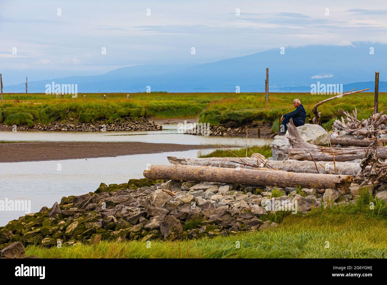 Uomo seduto su una grande roccia che guarda l'oceano da Garry Point Park a Steveston british Columbia Canada Foto Stock