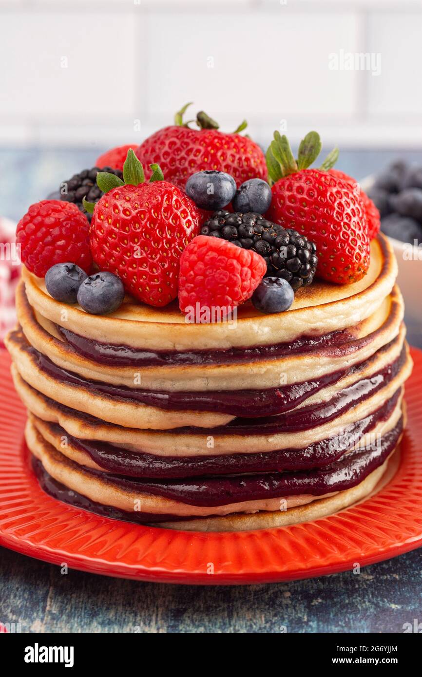 Stack di frittelle di Berry con Compote sparso su un rustico tavolo di legno blu Foto Stock