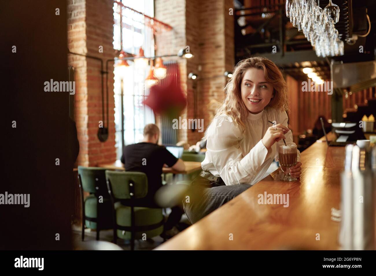Donna positiva seduta al bancone del bar e che beve caffè Foto Stock Donna positiva seduta al bancone del bar e che beve caffè Foto Stock