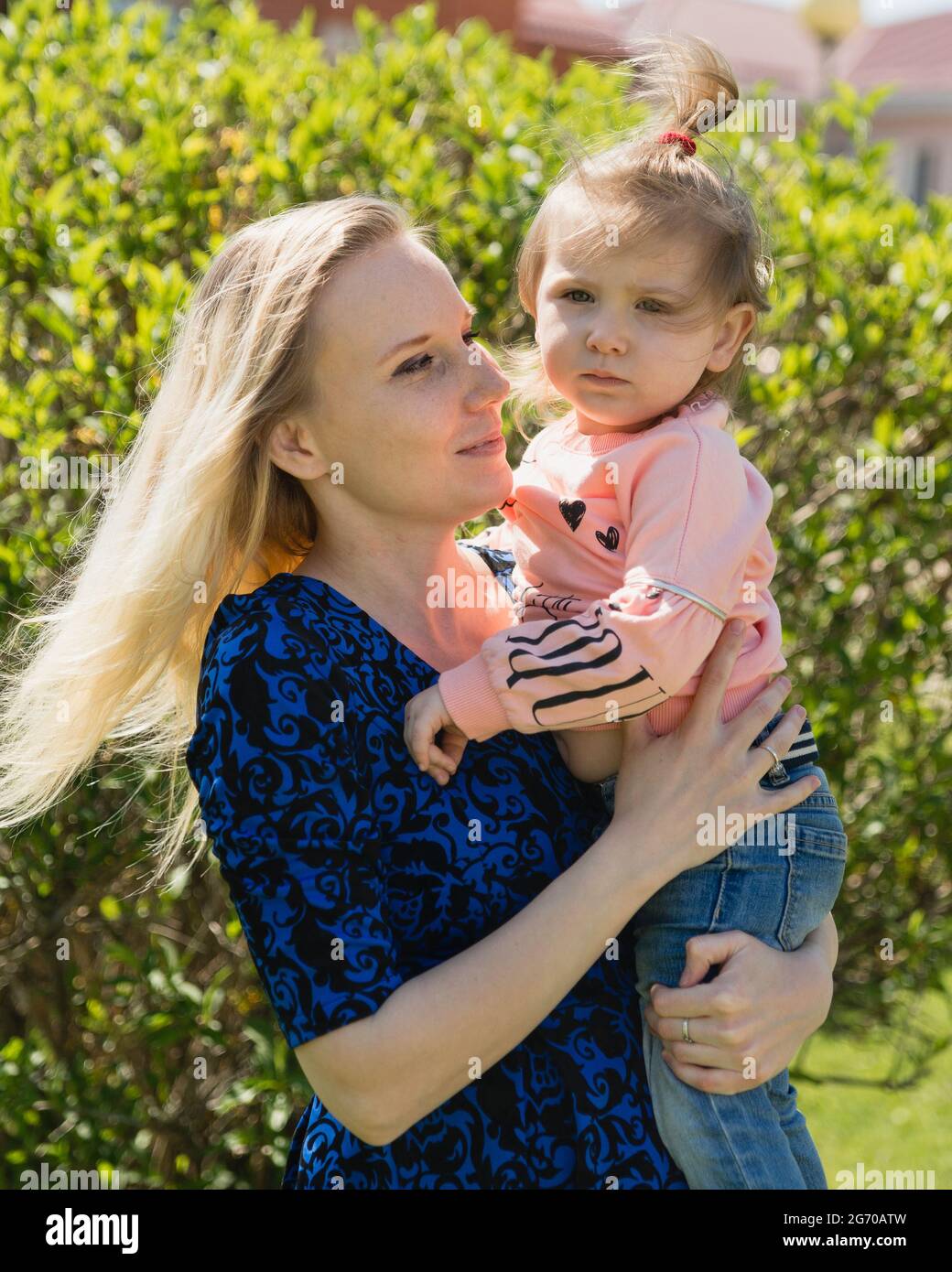 Una giovane bella madre guarda la figlia toddler. Una ragazza tra le braccia. Una giornata di sole. La felicità della maternità Foto Stock