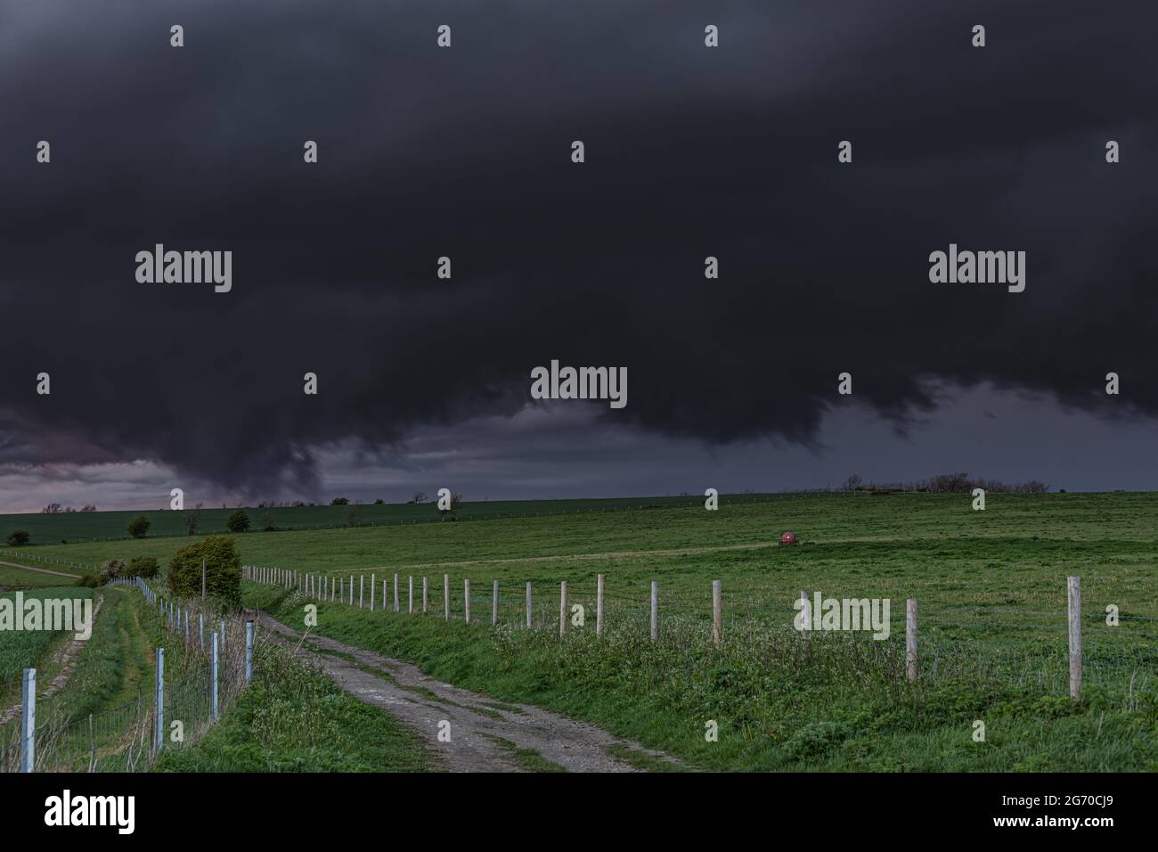 Percorso in un campo di erba su una fattoria con enormi nuvole nere che si preparano per un tornado nello sk Foto Stock