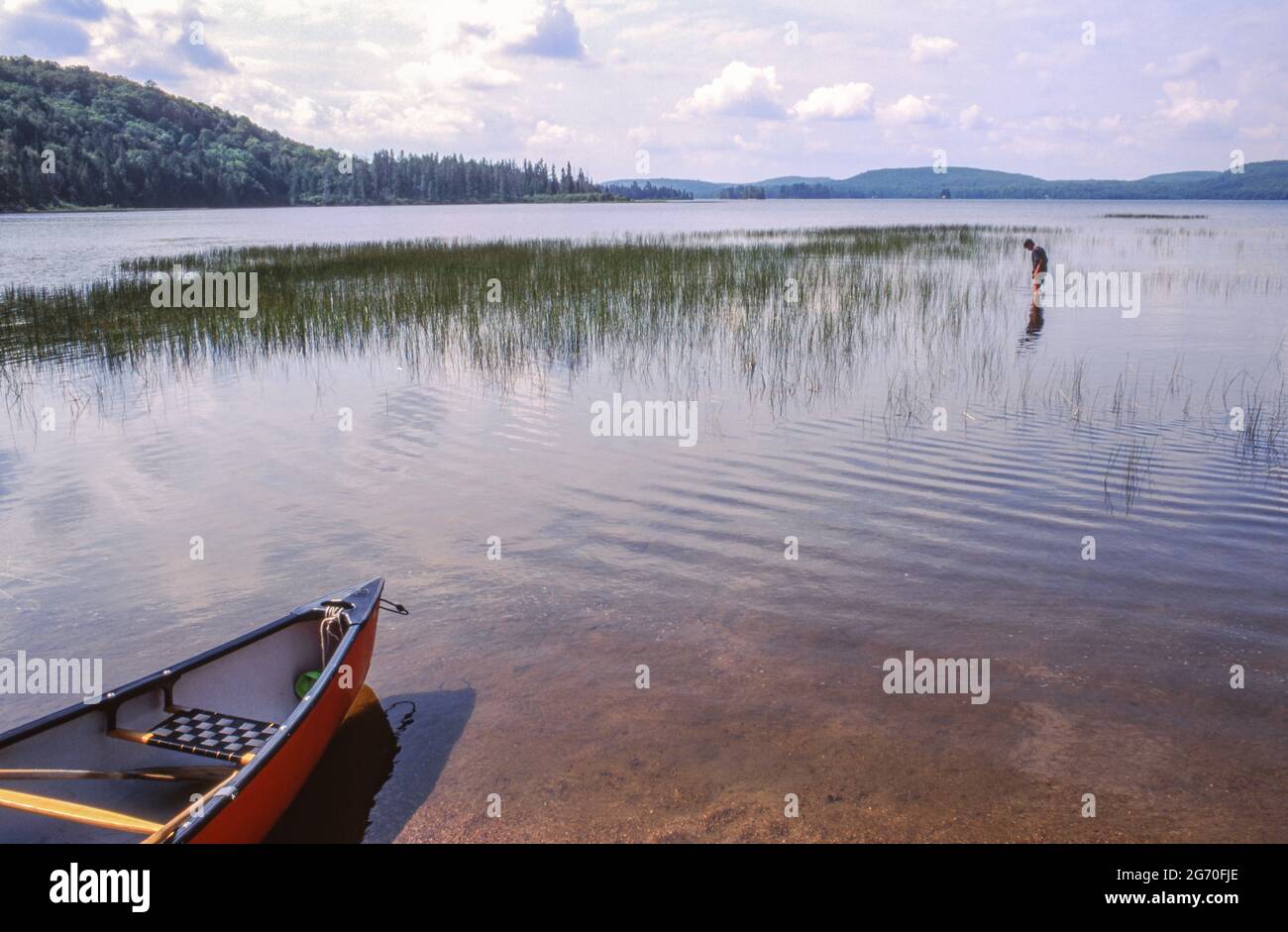 Una canoa ormeggiata e un ragazzo che guada in acque poco profonde sul lago Kawawaymog, Algonquin, Ontario, Canada. Foto Stock