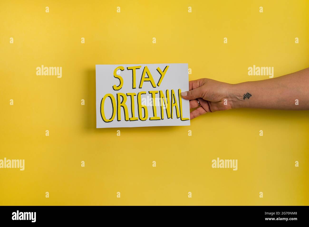 Un primo piano di una donna che tiene un foglio con la parola 'SAY ORIGINAL' su uno sfondo giallo Foto Stock