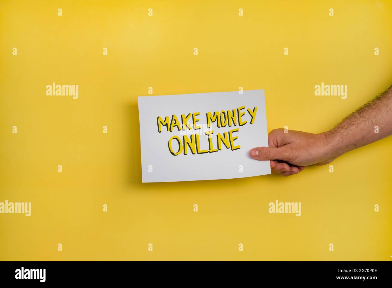 Un primo piano di un uomo che tiene una carta con la parola 'MAKE MONEY ONLINE' su uno sfondo giallo Foto Stock