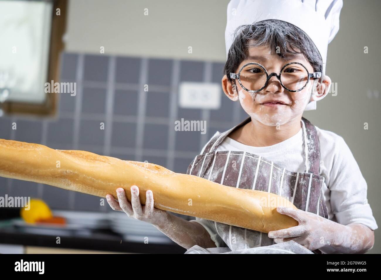 Asian Boy indossare bicchieri cucinare con farina bianca impastare impasto di pane insegna ai bambini pratica cottura ingredienti pane, uova su stoviglie in cucina l Foto Stock