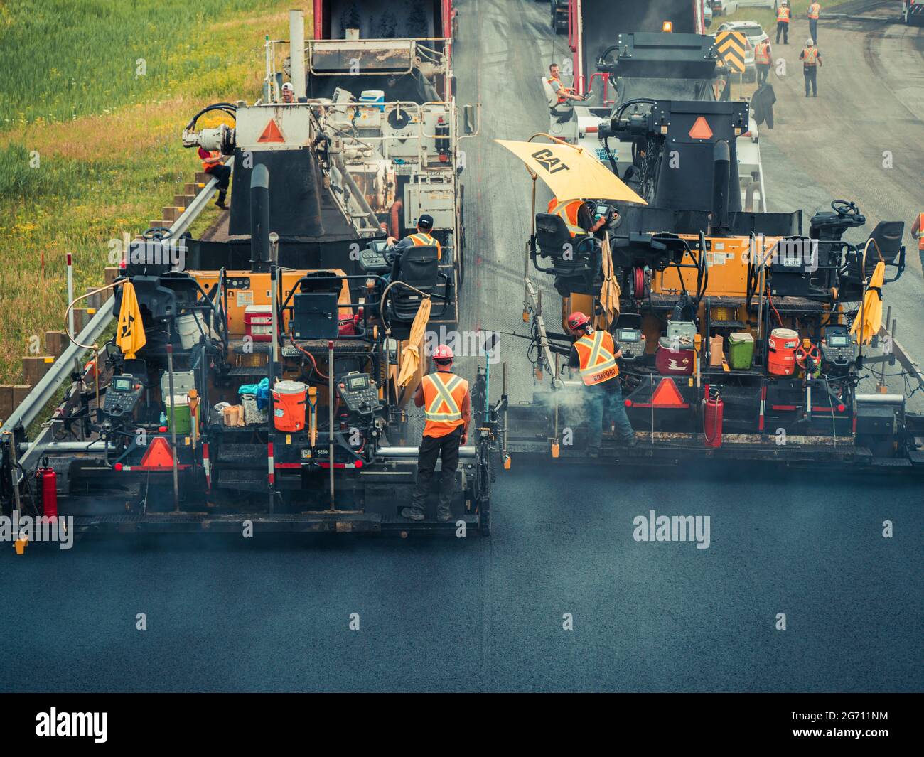 Uomini che lavorano più persone con cappelli duri e giubbotti arancioni riflettenti che utilizzano macchine per pavimentazione in asfalto CAT e dumper sulla strada statale 25 in Quebec. Foto Stock
