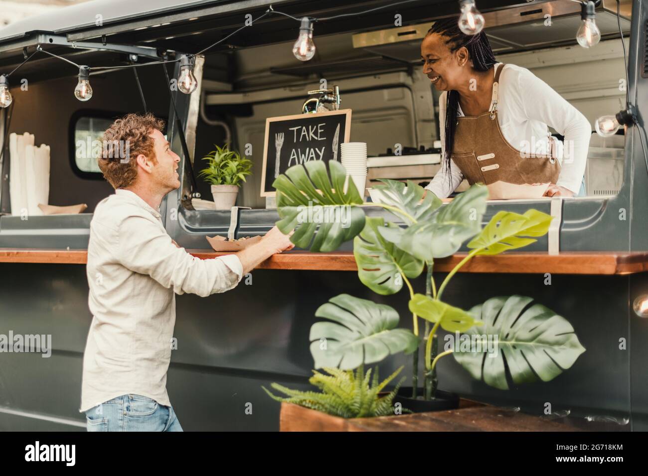 Donna chef africana che prende ordine dal cliente al camion del cibo all'aperto - Focus sul volto dell'uomo Foto Stock