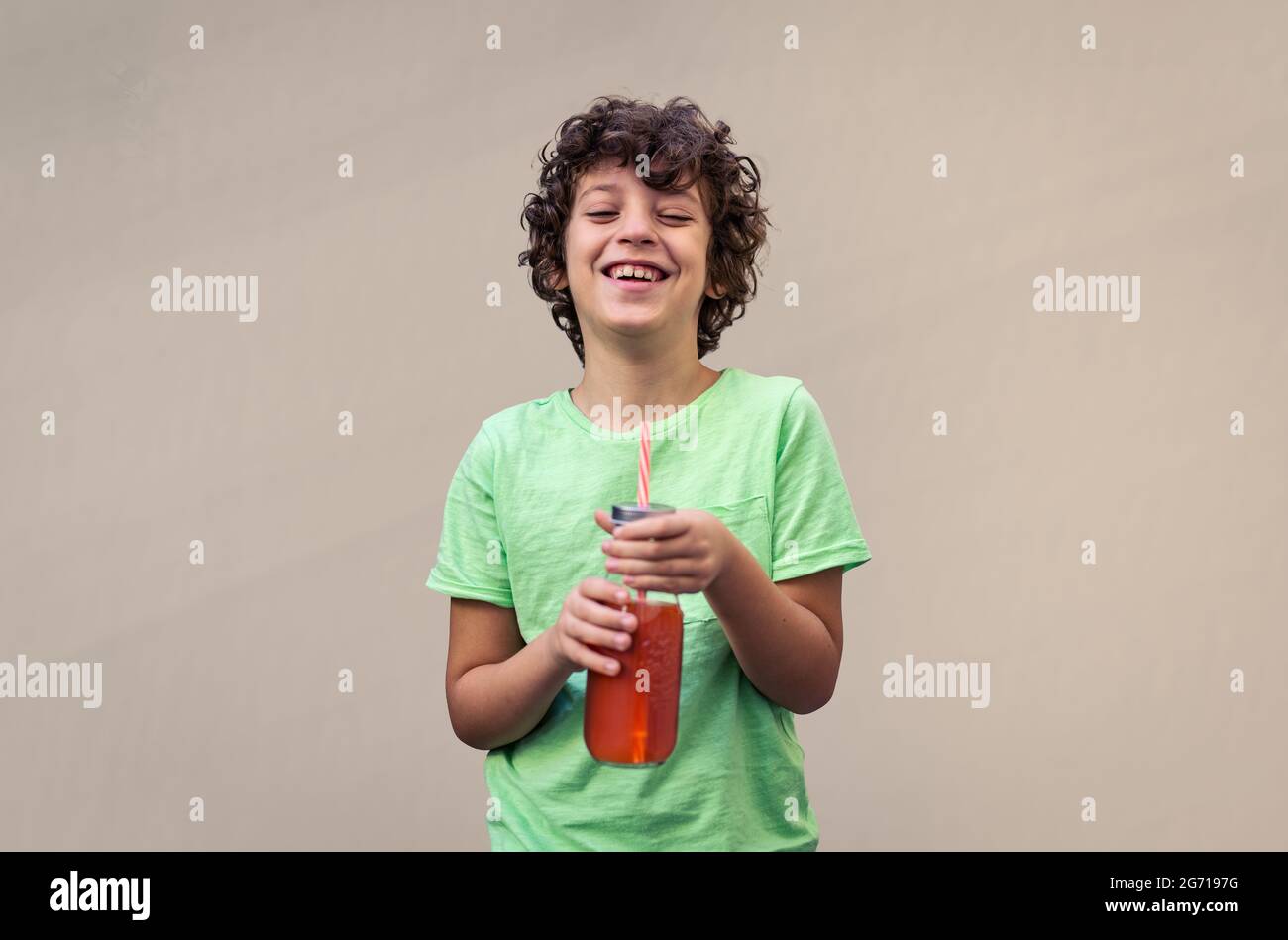 bambino di otto anni che tiene una bottiglia con un succo di frutta arancione e una paglia che sorride guardando la macchina fotografica. Foto Stock