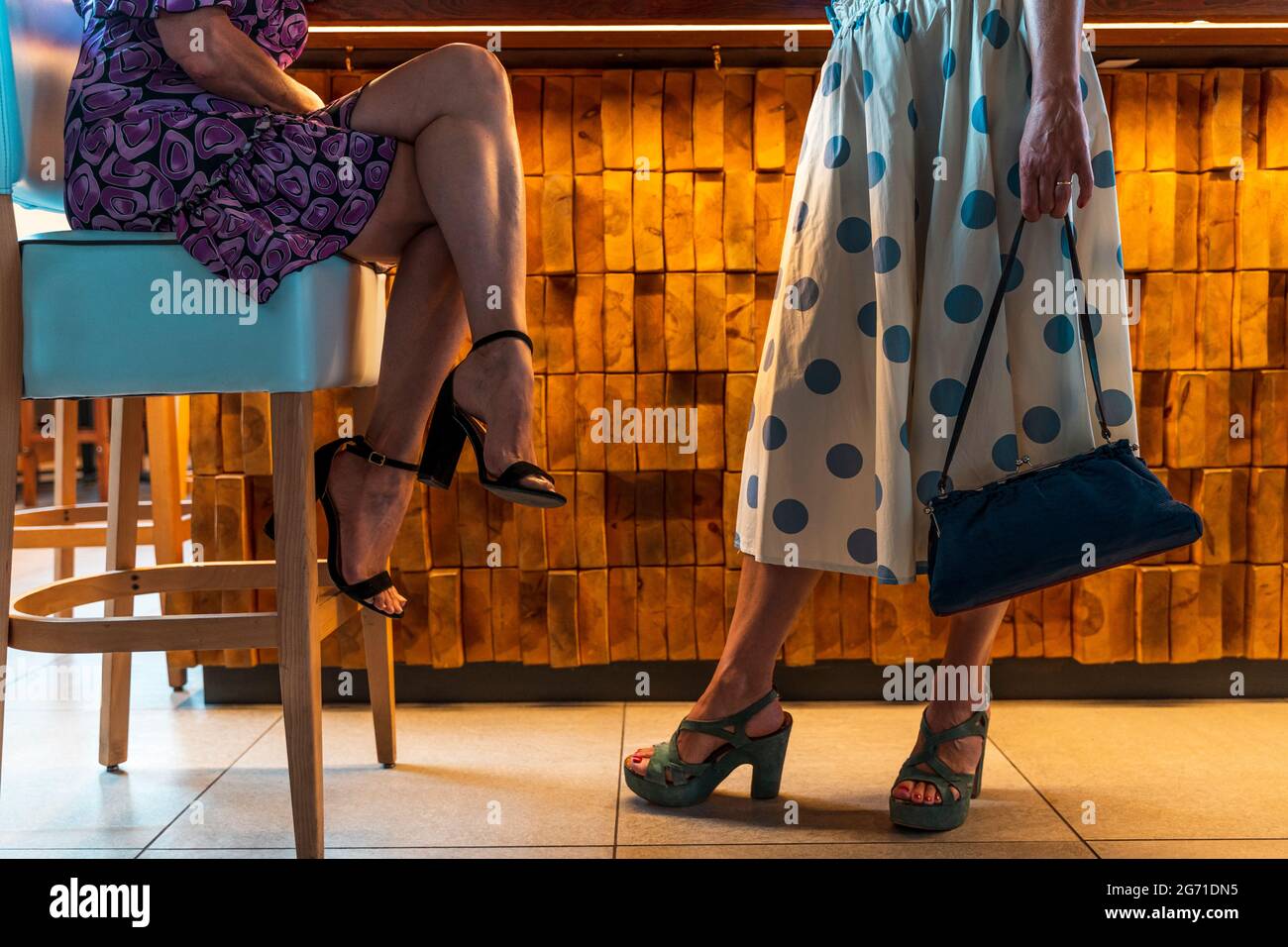 gambe di due donne elegantemente vestite di fronte a un bancone bar in un pub Foto Stock