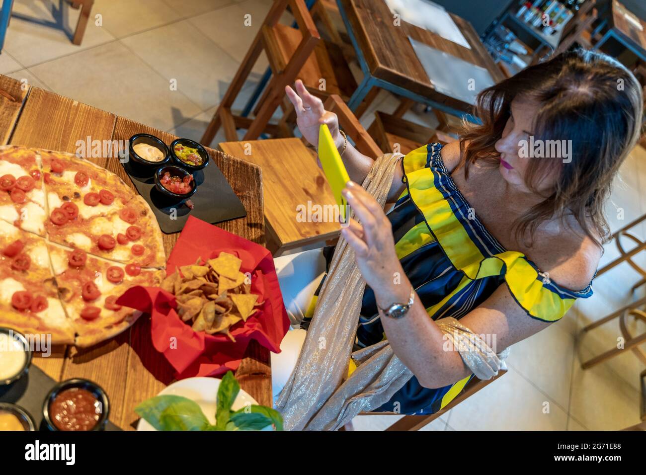 Elegante donna matura sta fotografando del cibo con smartphone su un tavolo in un pub Foto Stock