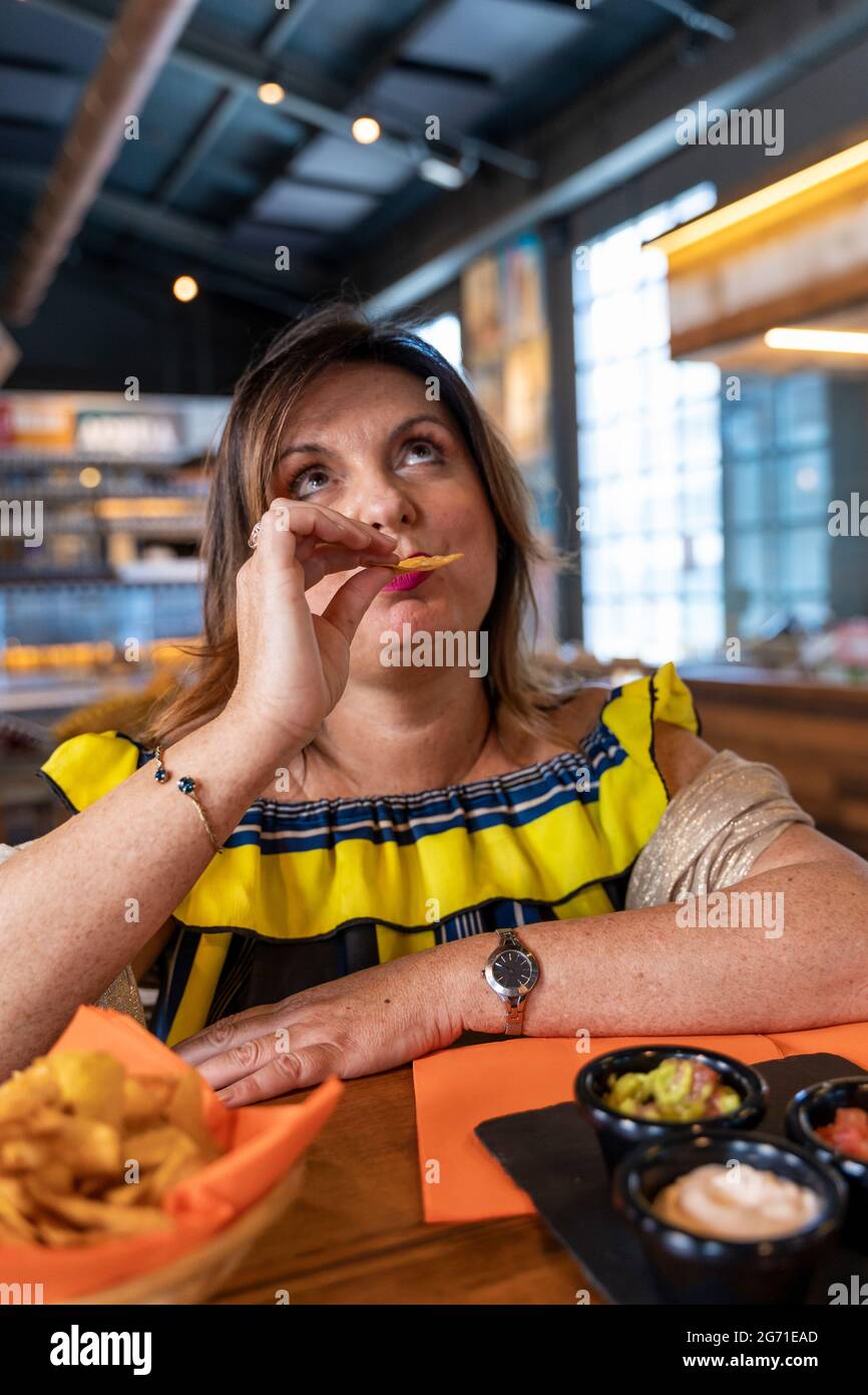 divertente ritratto di elegante donna matura sta mangiando una patata fritta in un pub Foto Stock