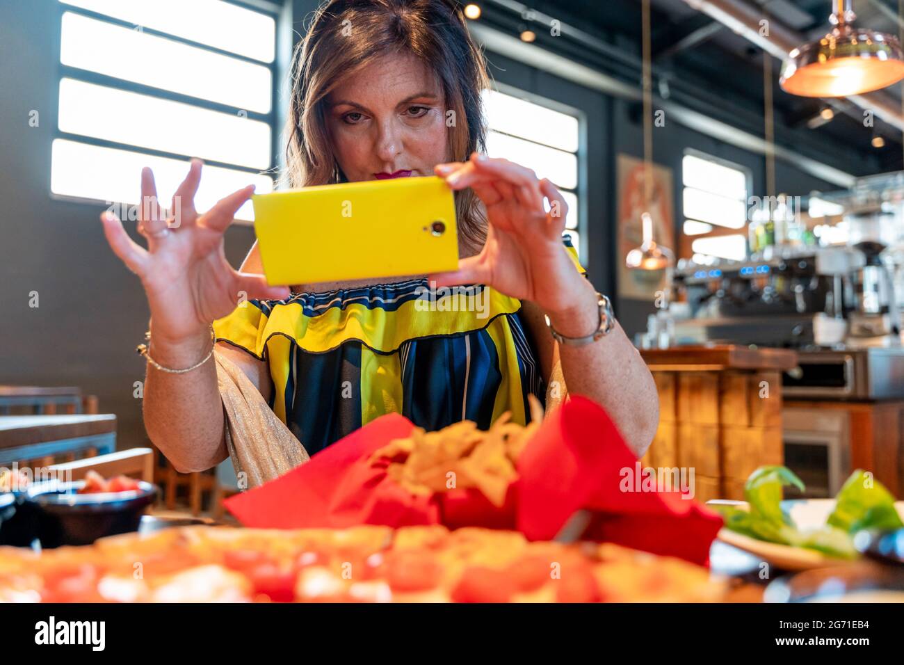 Elegante donna matura sta fotografando del cibo con smartphone su un tavolo in un pub Foto Stock