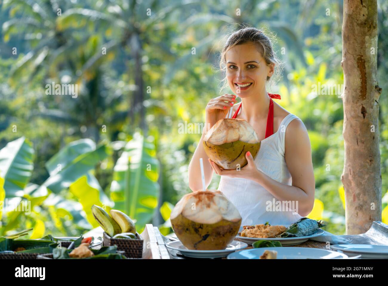 La donna nella giungla gazebo sorseggiando su una noce di cocco e mangiare cibi esotici Foto Stock