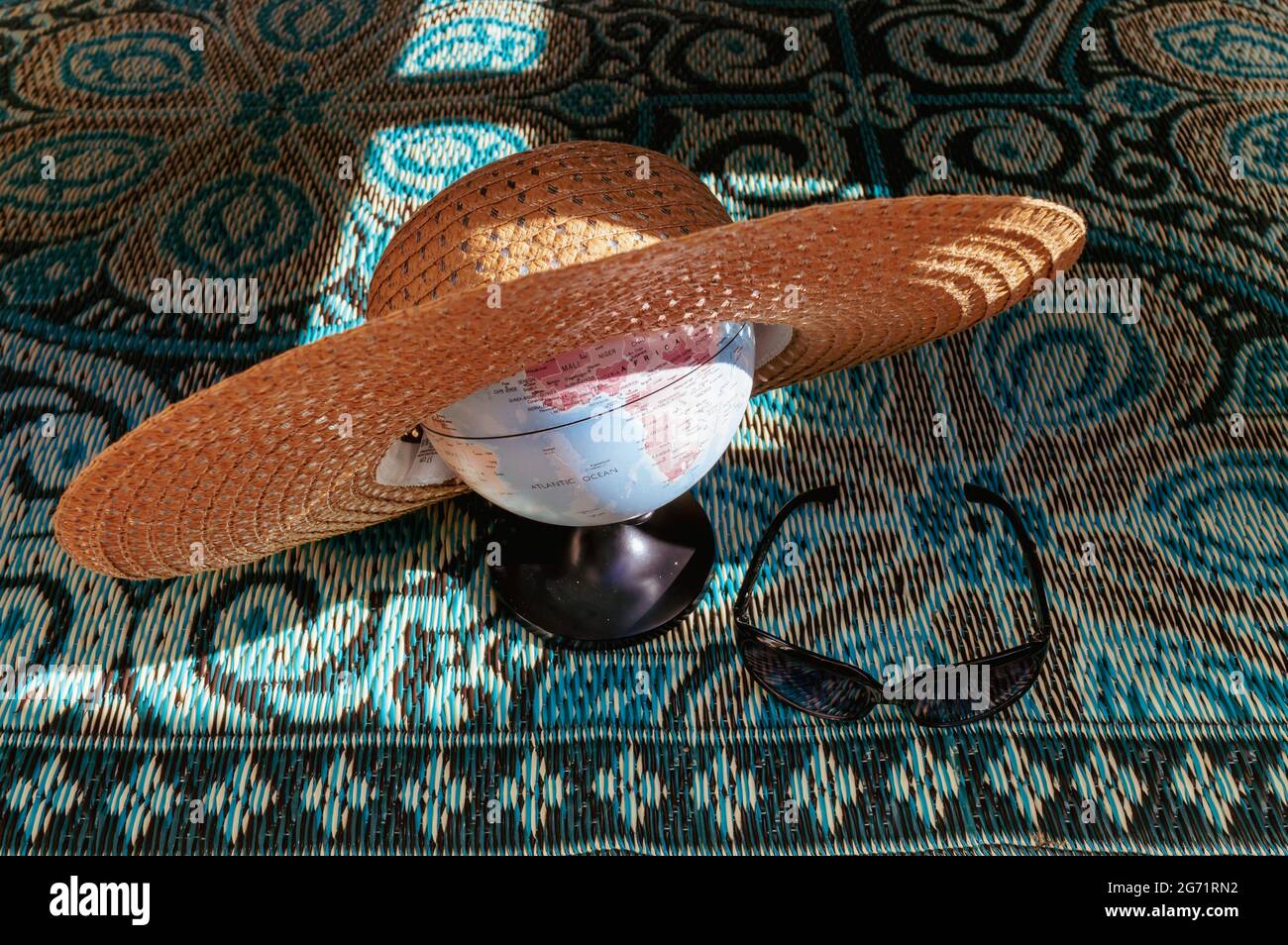 Immagine di un piccolo mondo globo che indossa un cappello estivo fatto di paglia su uno sfondo blu colorato Foto Stock