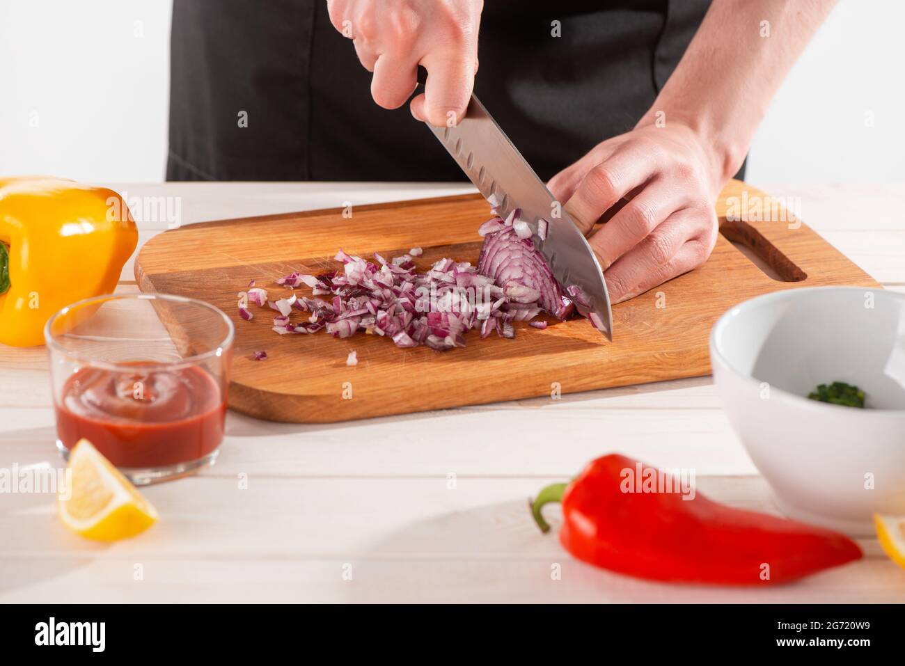 Primo piano sulle mani dello chef che tagliano la cipolla con un coltello santoku Foto Stock