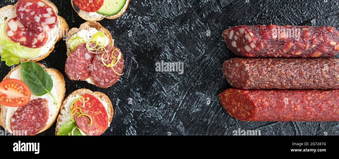 banner con vista dall'alto su sei panini o spuntini con salsicce e tre tipi di salsicce diverse su sfondo nero. posa piatta. Messa a fuoco morbida. Foto Stock