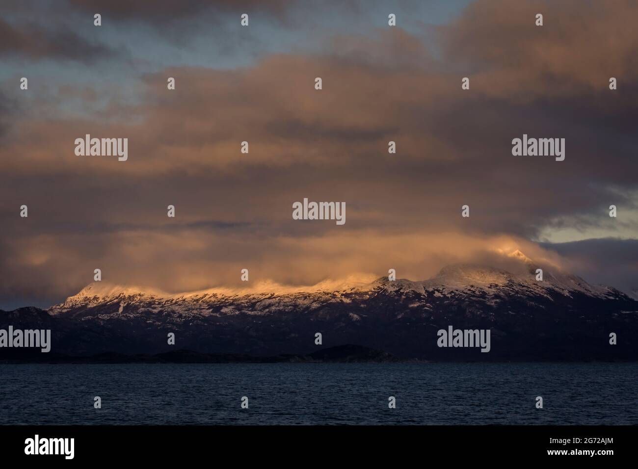 Sole sulle nuvole che sorvolano le vette di una piccola isola di Ushuaia, Tierra del Fuego, Argentina. Le acque sono del canale di Beagle. Foto Stock