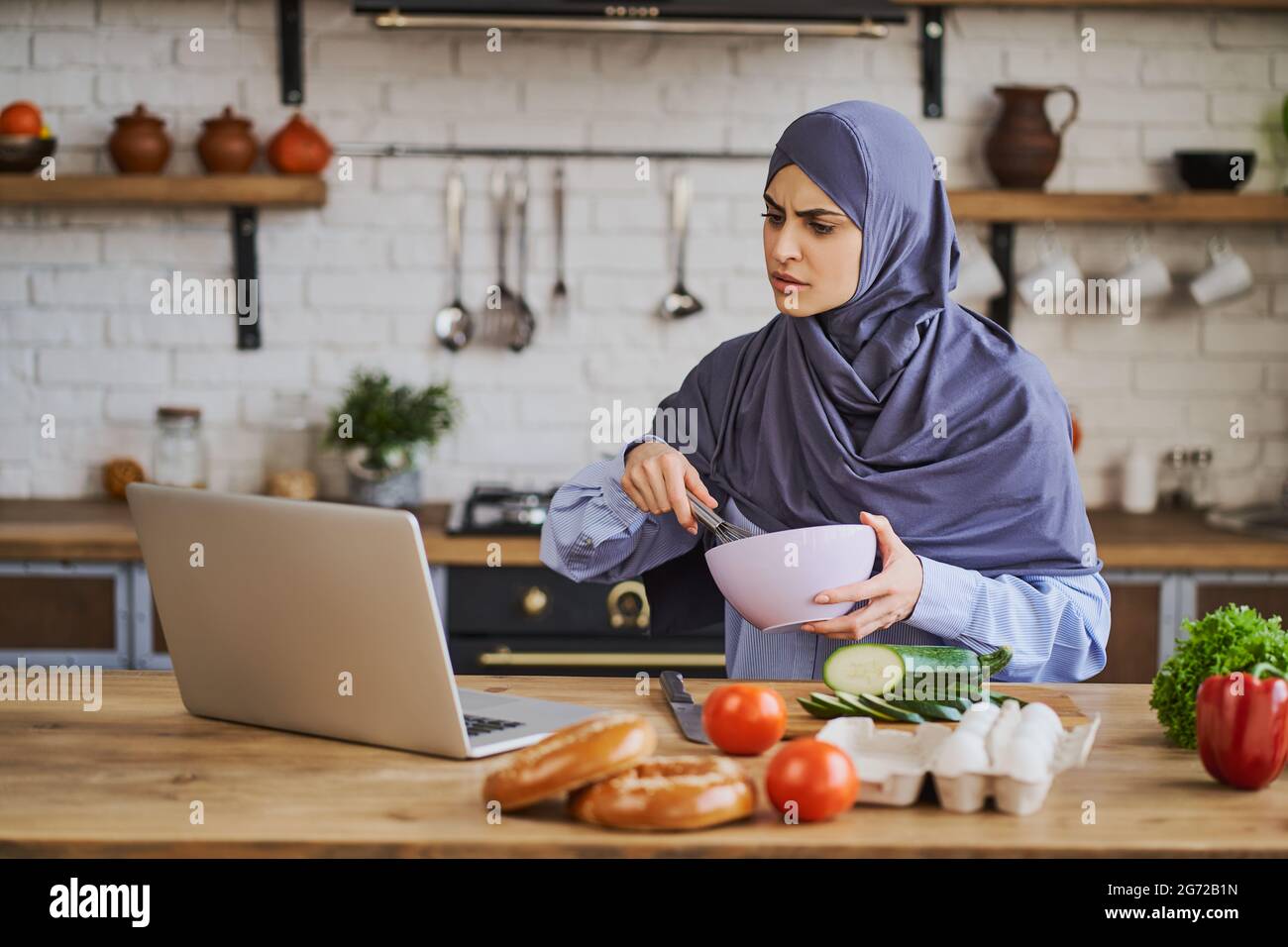 Donna araba che guarda un tutorial di cucina e frusta con un whisker Foto Stock