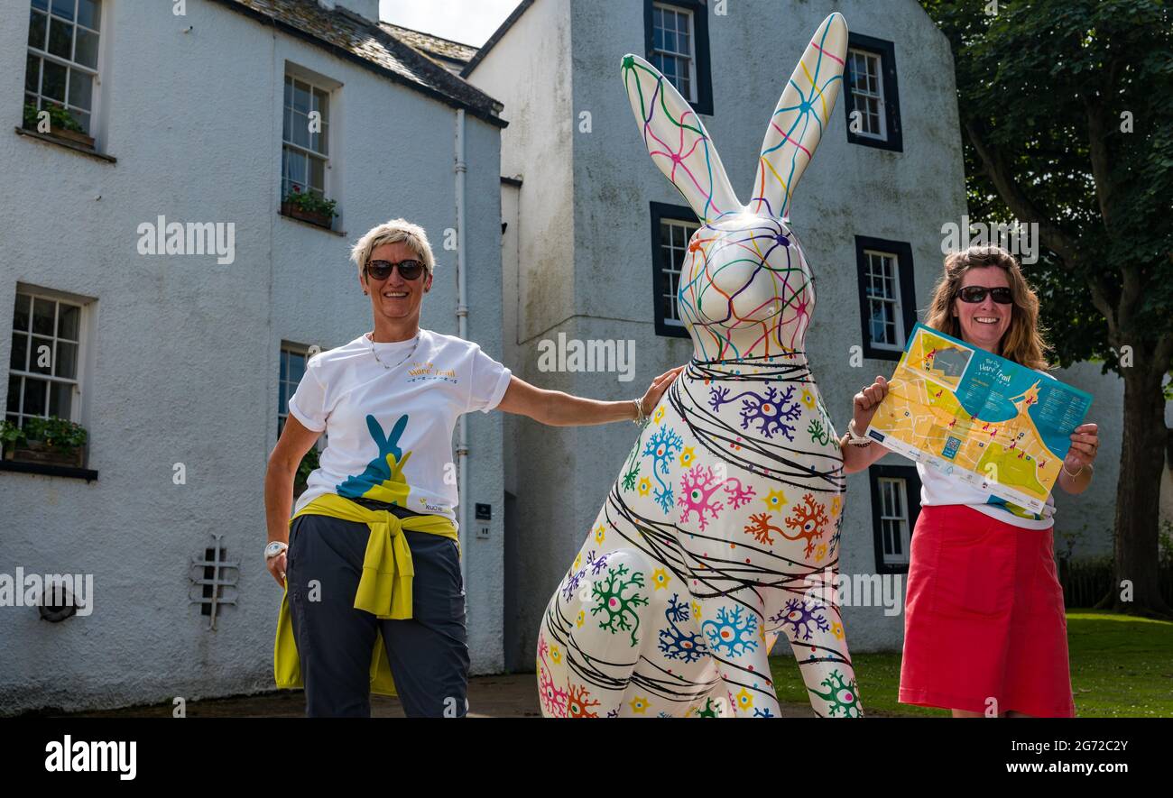 North Berwick, East Lothian, Scozia, Regno Unito, 10 luglio 2021. Il Big Hare Trail: Il sentiero inizia oggi e durerà 11 settimane con 10 gigantesche sculture di lepre dipinte a mano, ciascuna di un artista diverso, situate intorno alla città balneare. È organizzato da Leuchie House, una tregua di carità per le persone con disturbi neurologici. Nella foto: Volontari Helen e Fiona che aiutano con gli eventi in città con una lepre dipinta da Alison Blevins Foto Stock